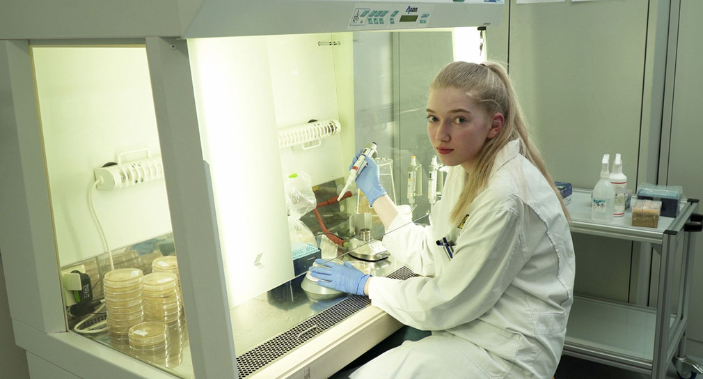Junge Frau sitzt im Labor und hält eine Pipette in der Hand.